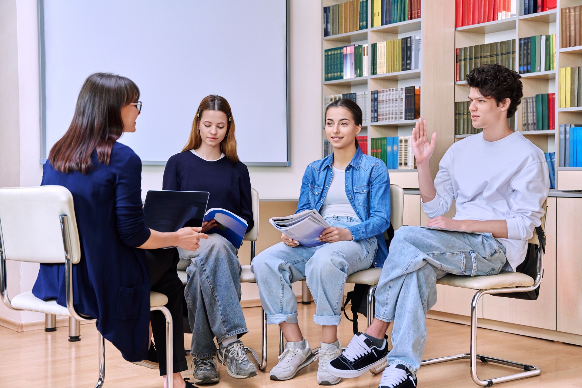 Group of teenage students with female teacher counselor inside classroom library